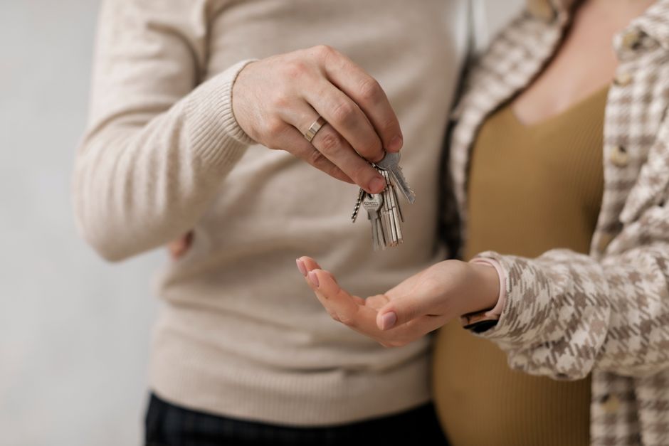 A close-up shot of a real estate agent handing house keys to a new homeowner in front of a modern, attractive house, symbolizing a successful sale.