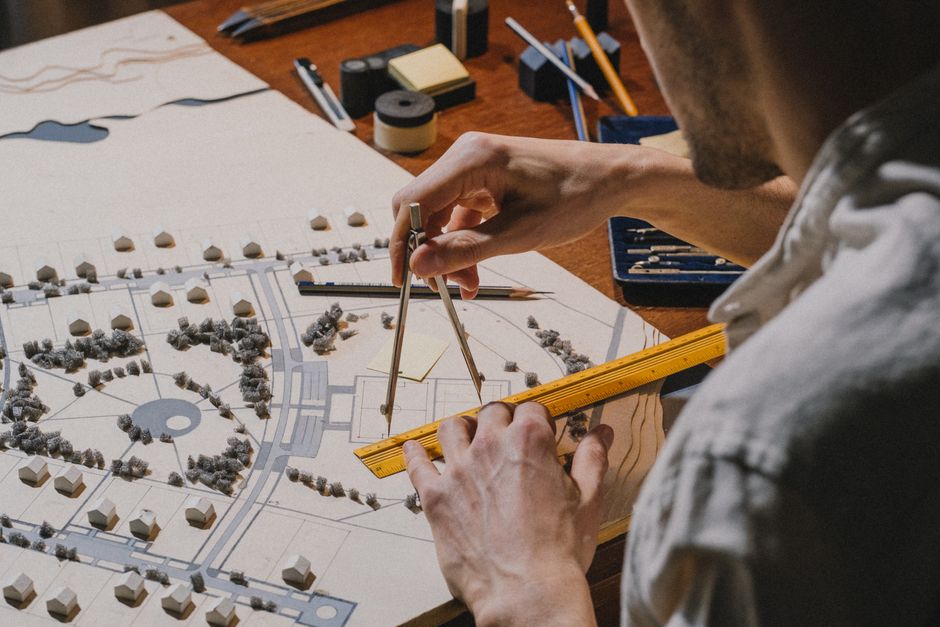 Focused individual sits at a modern, brightly lit desk, carefully reviewing architectural blueprints and taking notes for ...