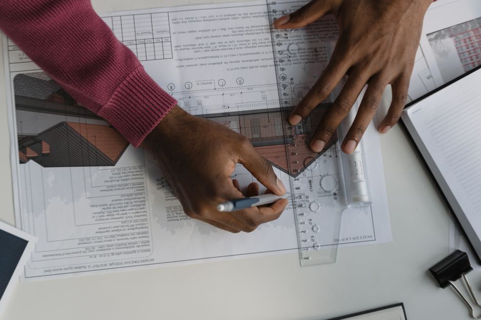 Focused professional in a bright, modern office meticulously studying architectural blueprints and real estate documents o...